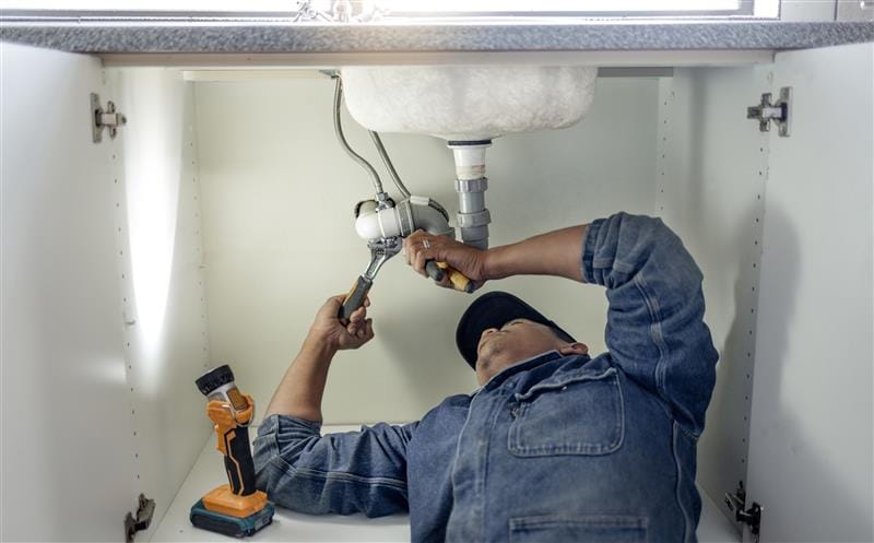 Plumber repairing pipes beneath a bathroom sink in Union City